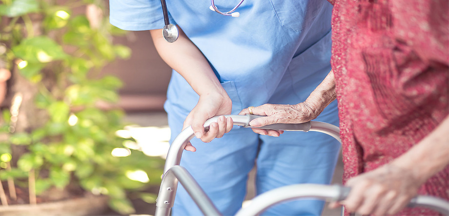 Medical Professional helping elderly patient with walker walk outside